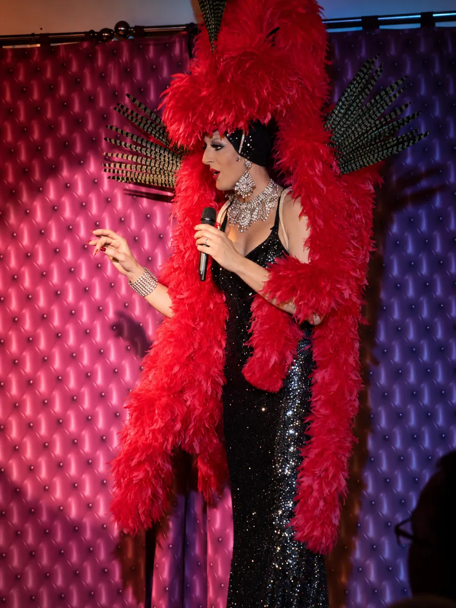 Lady Maxx en boa rouge et robe noire pailletée, au micro sur scène